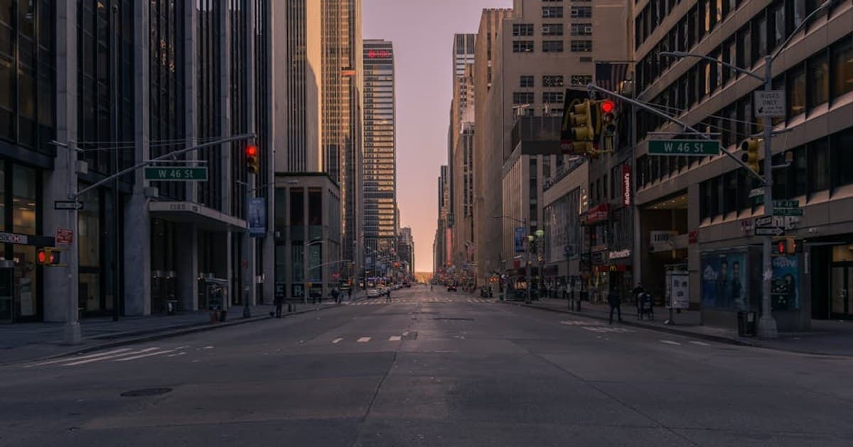 Empty New York City street at sunset with towering skyscrapers and soft glowing light.