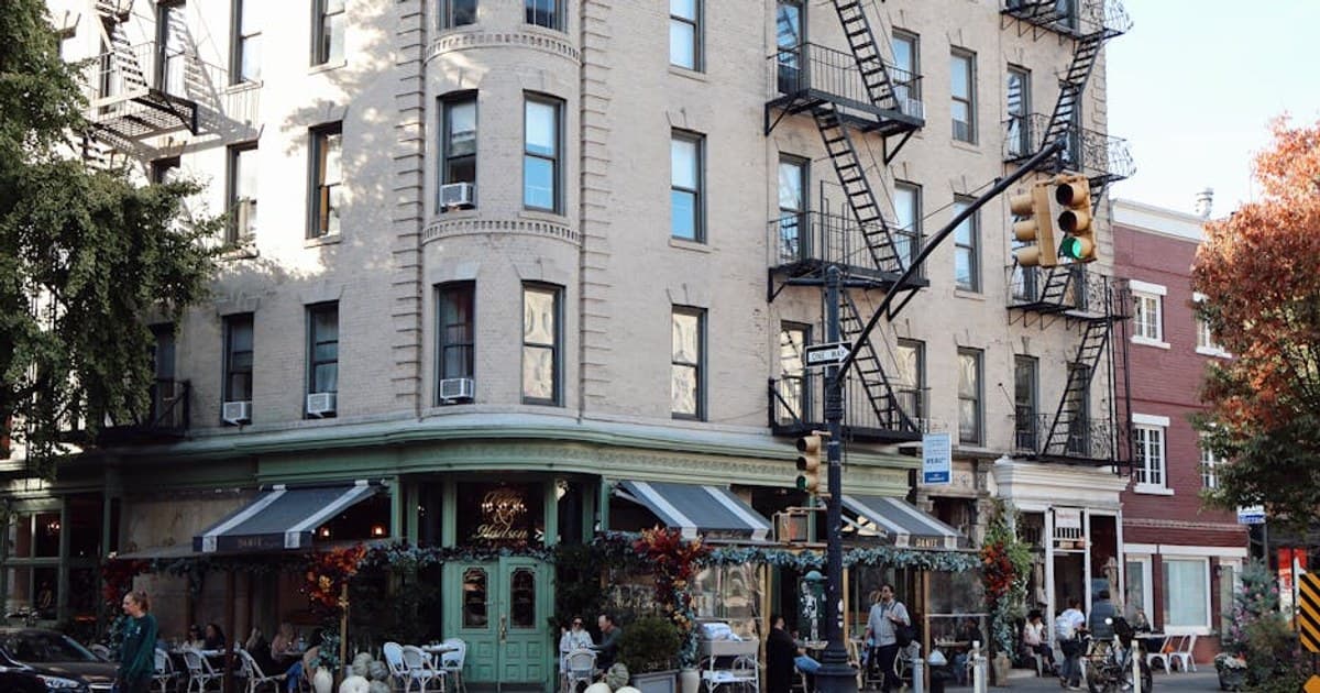 Street corner cafe in New York City with outdoor seating, typical urban architecture, and foot traffic.