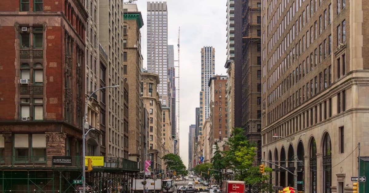 A busy street view of Midtown Manhattan with historic and modern buildings, pedestrians, and traffic.