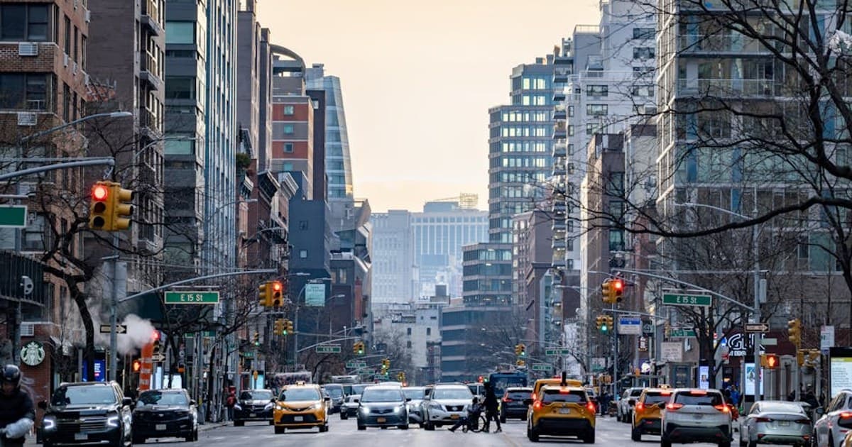 Bustling New York City street with skyscrapers at dusk, featuring yellow cabs and city life.