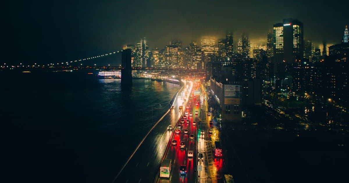 A dramatic view of a city at night with illuminated buildings and bridge under mist.