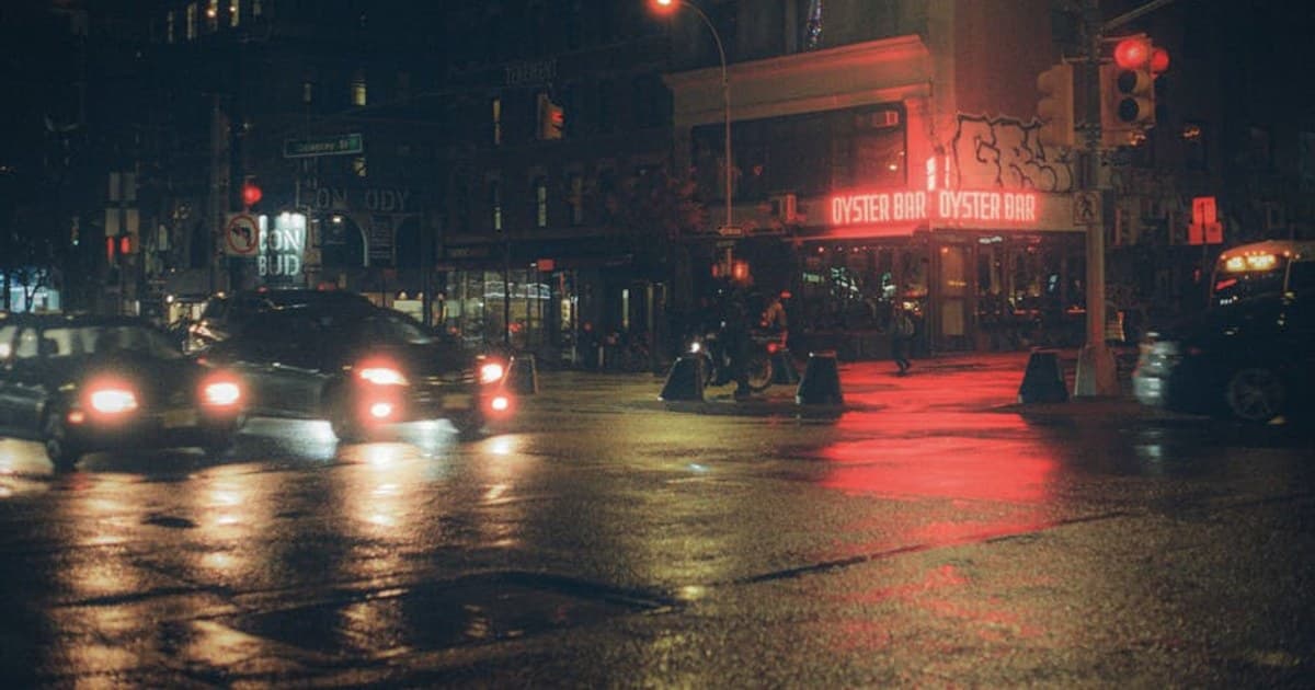 Glistening wet streets of NYC at night, featuring a vibrant oyster bar with red neon lights.