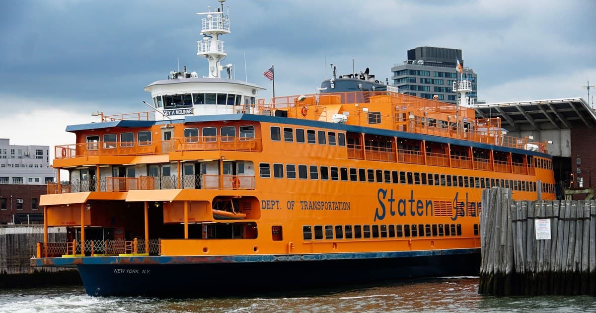 Vibrant orange Staten Island Ferry docked in New York Harbor under cloudy skies.