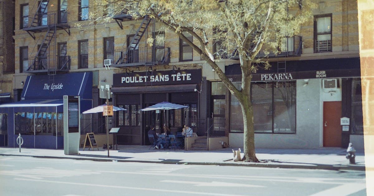 A sunny day street view of restaurants on Amsterdam Avenue, NYC, featuring outdoor seating.
